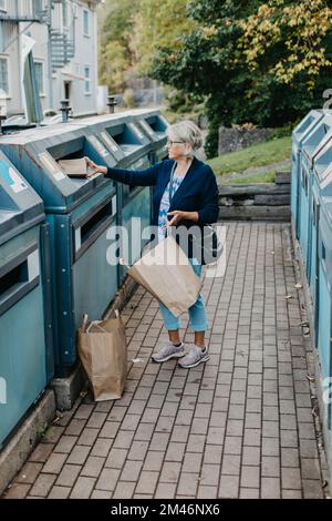 Woman putting cardboard in recycling bin Stock Photo