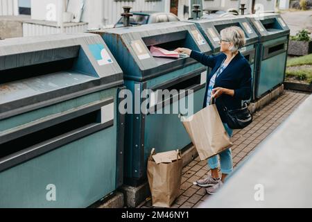 Woman putting paper in recycling bin Stock Photo