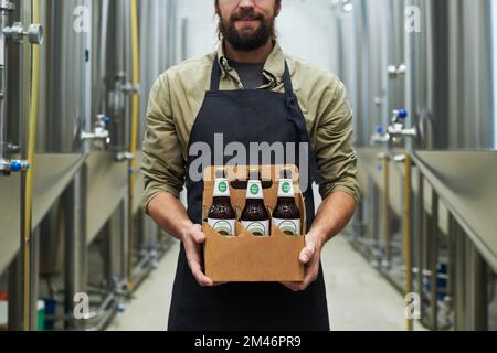 Cropped image of smiling brewer showing bottled beer produced in his brewery Stock Photo