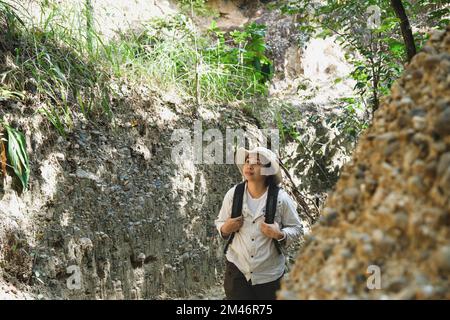 Female geologist with backpack exploring nature trail in forest and analyzing rock or gravel. Researchers collect samples of biological materials. Env Stock Photo