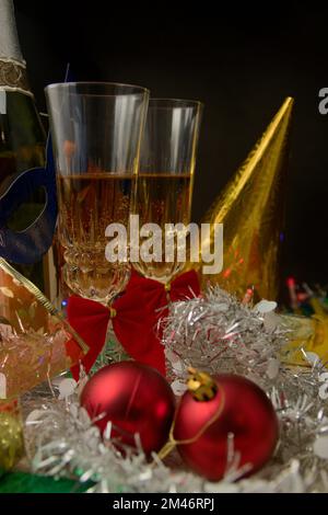 Two glasses of champagne on a table decorated with festive items such as brightly colored hats and masks and tinsel, to celebrate the end of the year Stock Photo