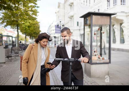 Colleagues walking in city and using phone Stock Photo
