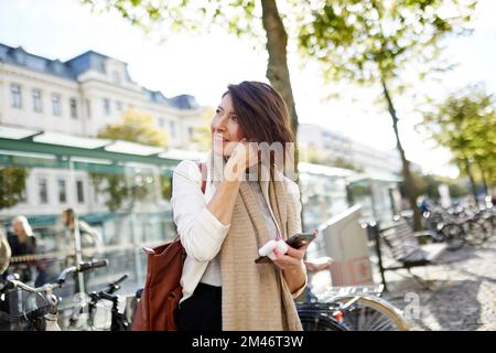 Smiling businesswoman using smart phone and earphones Stock Photo