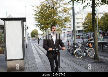 Businessman riding electric push scooter in city Stock Photo