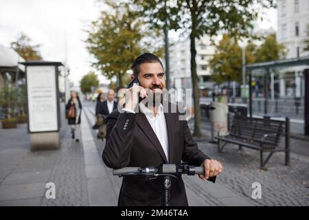 Businessman riding electric push scooter and talking on phone Stock Photo