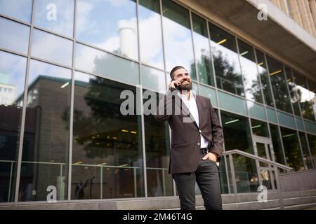 Smiling businessman talking on phone outside office building Stock Photo