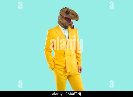 Portrait of guy in funky yellow suit and funny T Rex mask posing on blue background Stock Photo