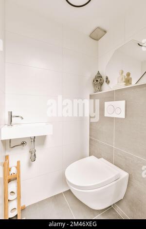 a white toilet in a bathroom with grey tiles on the walls and floor, along with a mirror above it Stock Photo