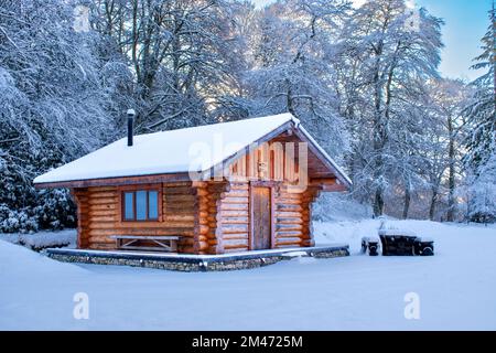 Logie Steading Forres Moray Scotland winter with snow covered trees and a wooden log chalet Stock Photo