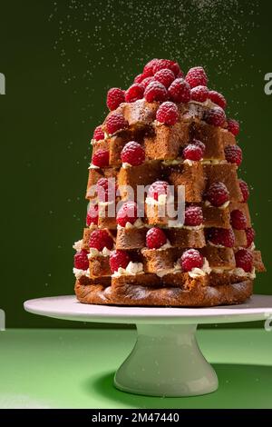 Christmas raspberry decorated Italian sweet bred Pandoro (pan d'oro) dusted with icing sugar on green background Stock Photo