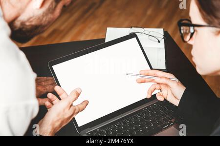 Two employees in office discussing business and pointing fingers at the screen of laptop. Stock Photo