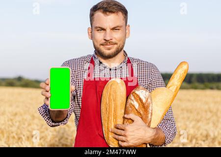 Baker man holding loaves of bread in his hand and showing the screen of his mobile phone. Stock Photo