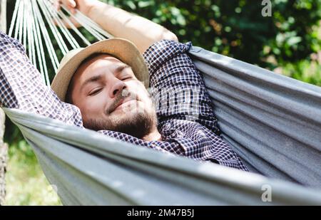 Bearded man in hat lying down on hammock. Stock Photo