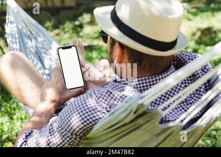 Man in hat using his smartphone while lying in hammock and relaxing. Stock Photo