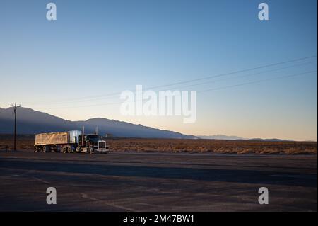 American Peterbilt long nose truck with a large trailer driving on the deserted roads at sunset Stock Photo