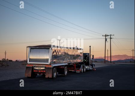 American Peterbilt long nose truck with a large trailer driving on the deserted roads at sunset Stock Photo