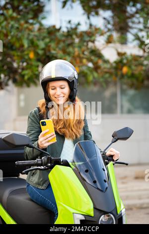 Red-haired woman on her motorcycle using smart phone Stock Photo
