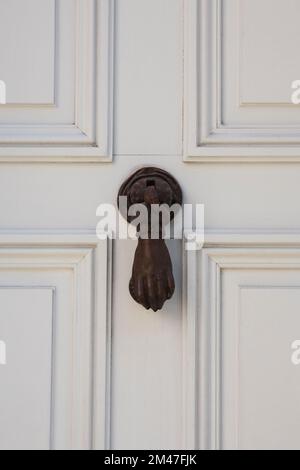 Black hand door knocker on a white wooden door. Stock Photo