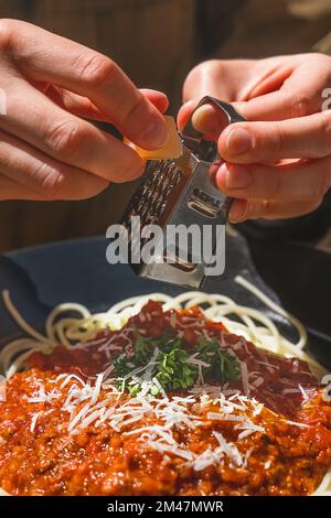 https://l450v.alamy.com/450v/2m47mwr/hands-grating-delicious-parmesan-cheese-on-freshly-made-italian-bolognese-pasta-small-box-of-cheese-grater-italian-cuisine-bolognese-pasta-recipe-2m47mwr.jpg