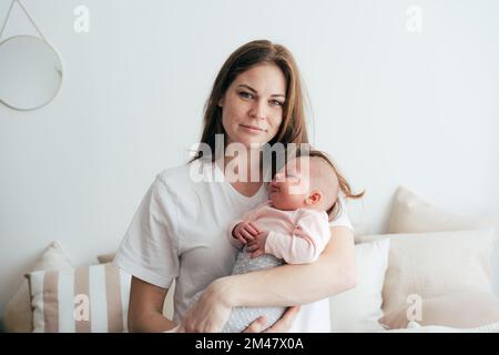 Portrait of a young attractive red-haired mother holding and hugging her newborn daughter. Stock Photo