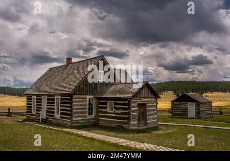 Old historic log cabins stand in a Colorado high country meadow beneath the stormy skies of a late summer day. Stock Photo