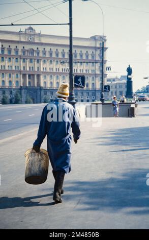 Historical, Archival Image Of A Government Street Cleaner With Bucket Walking Towards The Lubyanka Building And The Statue Of Felix Dzerzhinsky, Iron Felix That Was Removed In 1991 And Moved To The Fallen Monument Park, Muzeon Park Before The Dissolution Of The Soviet Union, Moscow Russia 1990 Stock Photo