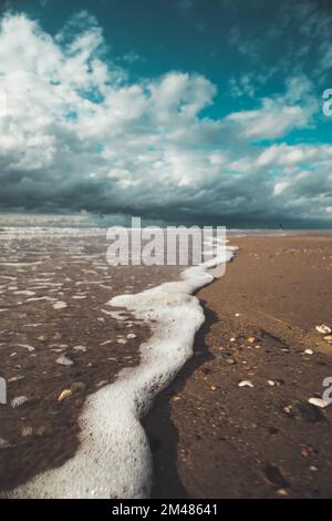 A closeup shot of bubbling waves washing the coast under the blue sky and clouds Stock Photo