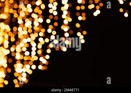 Festive bright blurred golden background. On Christmas black curtain, yellow bokeh lights are shining out of focus. Blank for postcards, place for tex Stock Photo