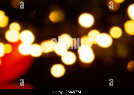 Bright, blurry lights on a Christmas tree from a garland. Festive yellow bokeh out of focus on black background. Street decoration, macro concept. Cit Stock Photo