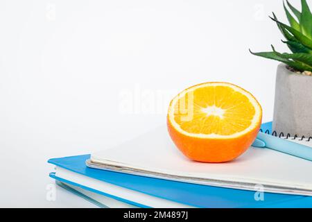 Notebooks and an orange on a white background, isolated, copy space. Stock Photo