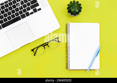Laptop, glasses and blank notepad on green background, flat lay. Stock Photo