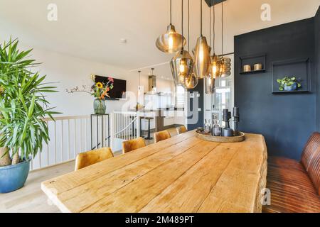 a dining room with a wooden table and some plants in pots on the wall next to the kitchen is dark blue Stock Photo