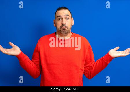 Caucasian bearded man isolated on blue background doubting and shrugging in questioning gesture Stock Photo