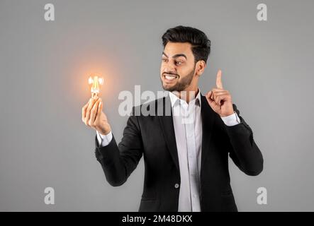 Ideas And Innovations. Portrait Of Young Arab Businessman Holding Illuminated Light Bulb Stock Photo