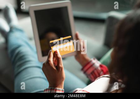 Busy millennial black female use credit card and tablet with empty screen, ordering goods remotely Stock Photo