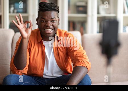 Positive cool black guy vlogger streaming from home, using phone Stock Photo