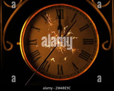 Sparkler in front of old golden vintage clock with roman numerals at 12 o'clock, New Year's Eve celebration background Stock Photo
