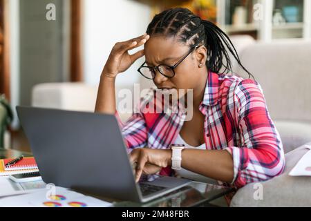 Depressed upset african female sit at workplace, using computer Stock Photo