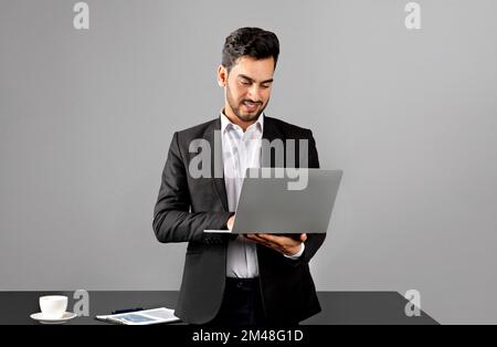 Portrait Of Smiling Arab Businessman In Suit Using Laptop In Office Stock Photo