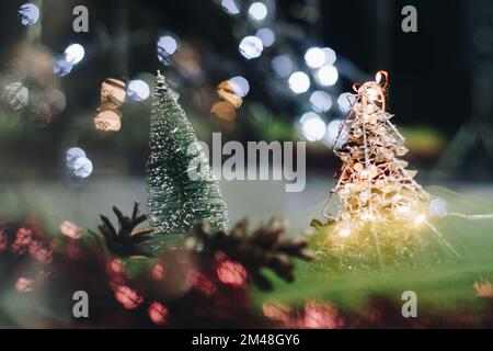 Christmas and New Year's card with a small artificial green tree and cones on a table with a colorful background in which lights shine, creating a bok Stock Photo