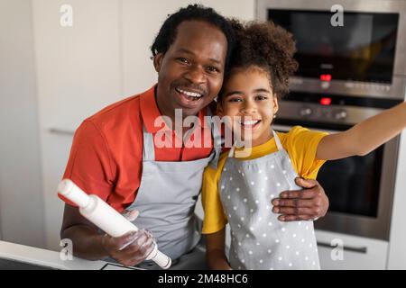 Cute Black Girl Taking Selfie With Her Dad While Cooking In Kitchen Stock Photo