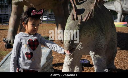 Woodland Hills, USA. 19th Dec, 2022. A girl touches a life-sized dinosaur at an exhibition named 'Dinosaurs in the Valley' in Woodland Hills, California, the United States, on Dec. 18, 2022. A large-scale dinosaur exhibition is being held in Woodland Hills in Southern California, attracting visitors to interact with life-sized animated dinosaurs. Credit: Zeng Hui/Xinhua/Alamy Live News Stock Photo