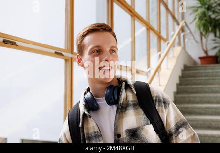 Smiling guy with headphones standing in college and looking away Stock Photo