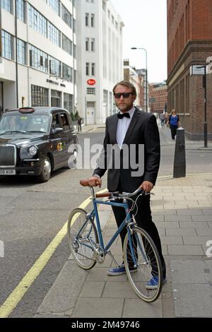 man dressed in tuxedo standing beside bicycle Stock Photo