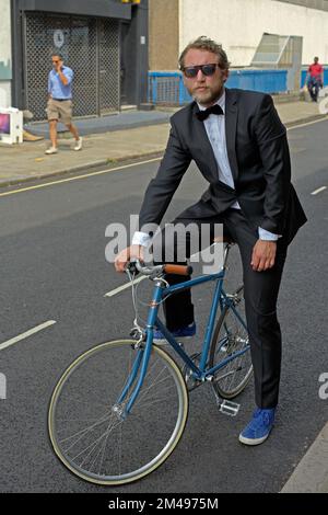 man dressed in tuxedo standing beside bicycle Stock Photo