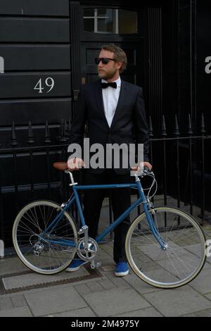 man dressed in tuxedo standing beside bicycle Stock Photo