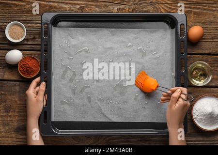 Woman greasing baking paper with oil on wooden background Stock Photo