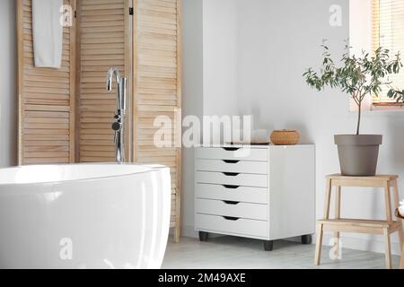 Modern bathtub and chest of drawers near white wall in bathroom interior Stock Photo