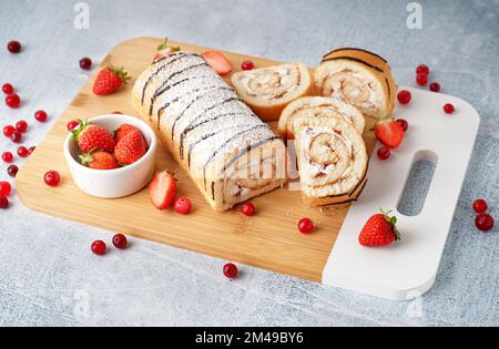 Cutting board with delicious sponge cake roll and fresh berries on light table Stock Photo