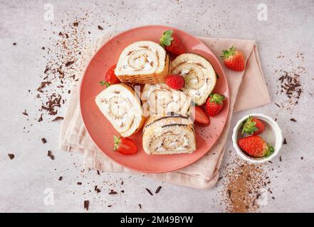 Pink plate with pieces of delicious sponge cake roll, fresh strawberries, napkin and chocolate on light background Stock Photo